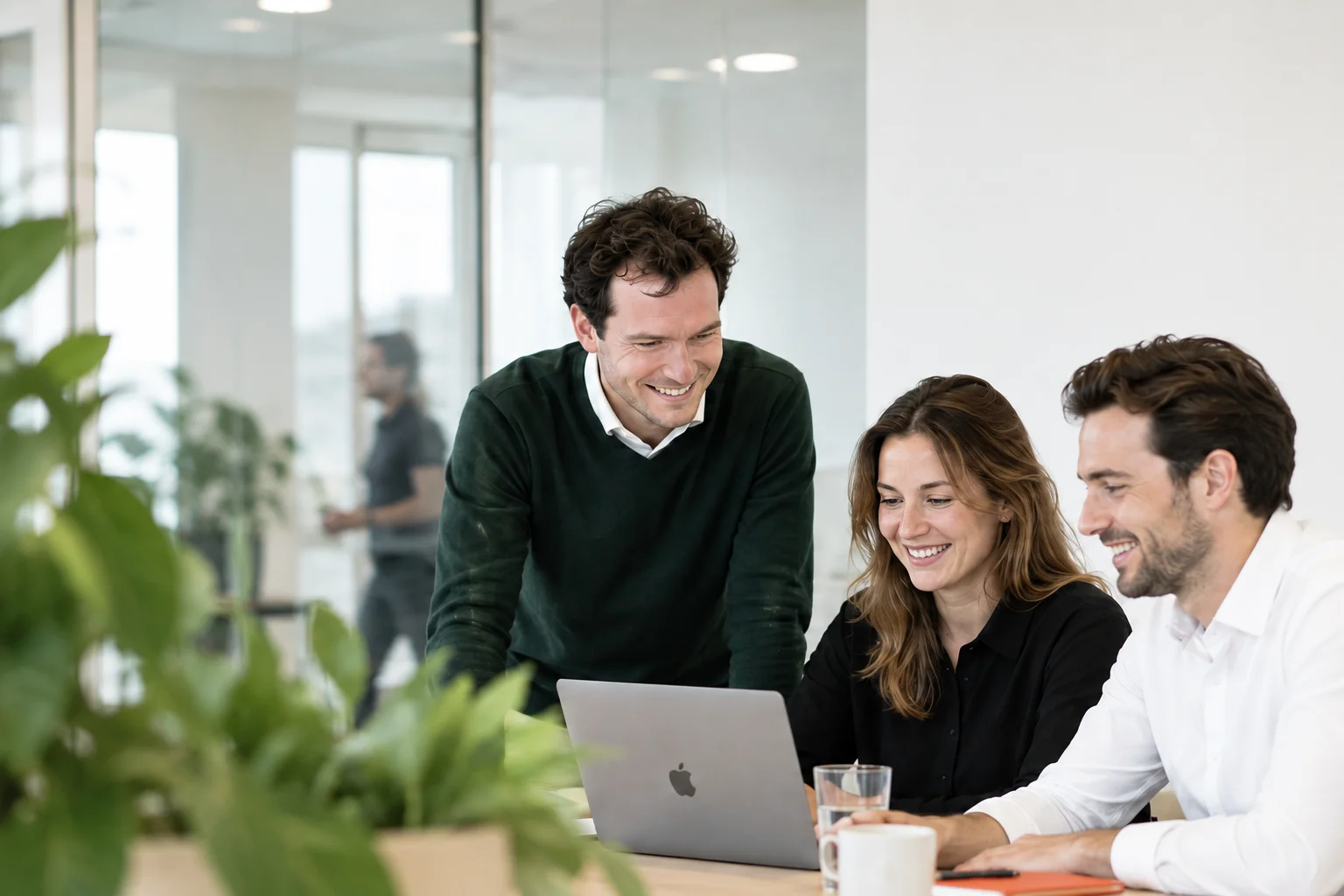 Drie collega’s werken samen aan een laptop in een licht kantoor.